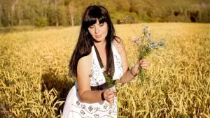 Brunette woman in a summer dress picking wildflowers in a sunny field.