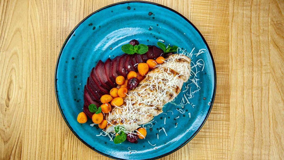 Delicious grilled chicken with vegetables and cheese on a vibrant blue plate.